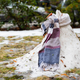 A melting snowman wearing a scarf surrounded by dirt